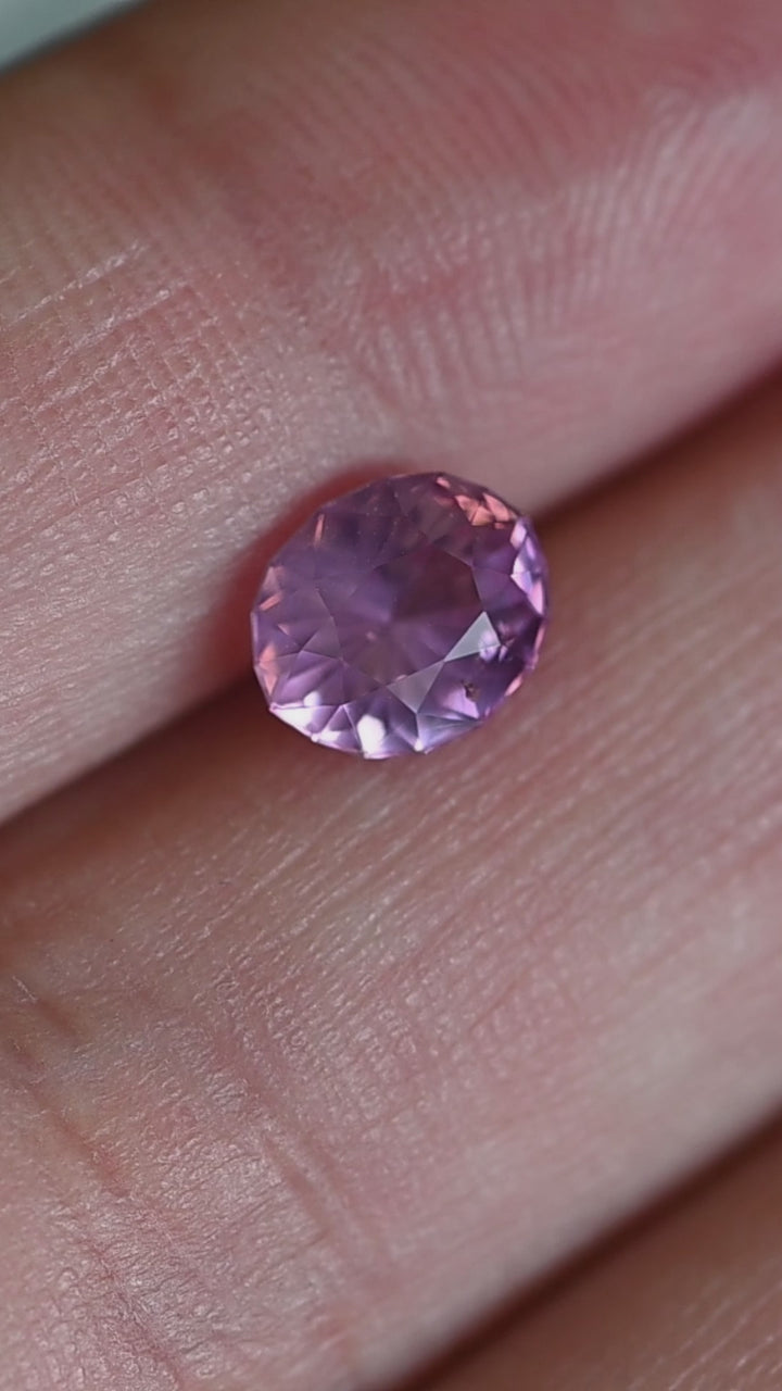 1.61 carat opalescent vivid pink oval sapphire rotating in hand under natural light