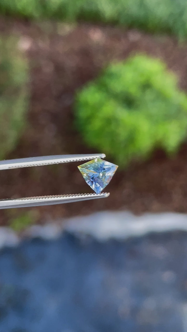 A mesmerizing 360-degree view of a 1.58-carat bi-color yellow and cornflower blue sapphire, showcasing its intricate shield cut and brilliance under natural light.