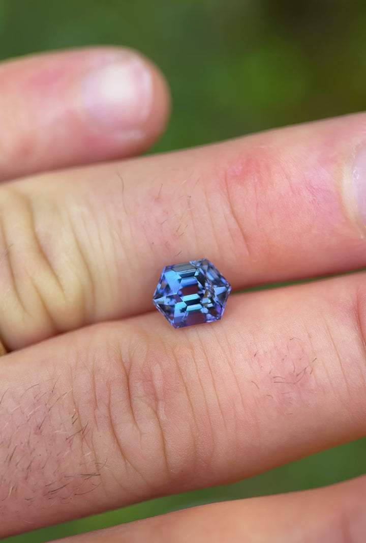 Handheld video of a natural 2.28 carat Tanzanite showing teal and violet hues in a hexagon step cut, filmed in outdoor daylight.