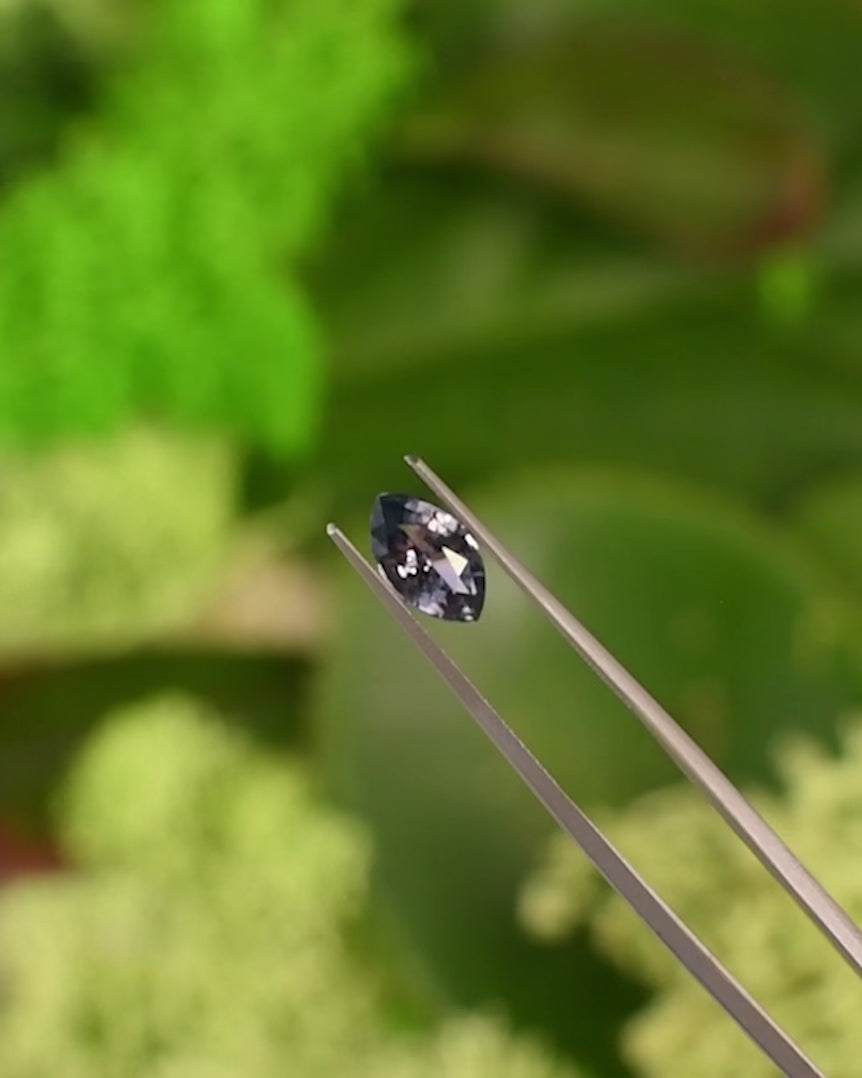 Video of 1.68CT pinkish gray violet sapphire rotating in gemstone tweezers, showing flashes of light and subtle color shift between violet and gray hues in the precision marquise mixed cut, unheated sapphire from Sakaraha, Madagascar.