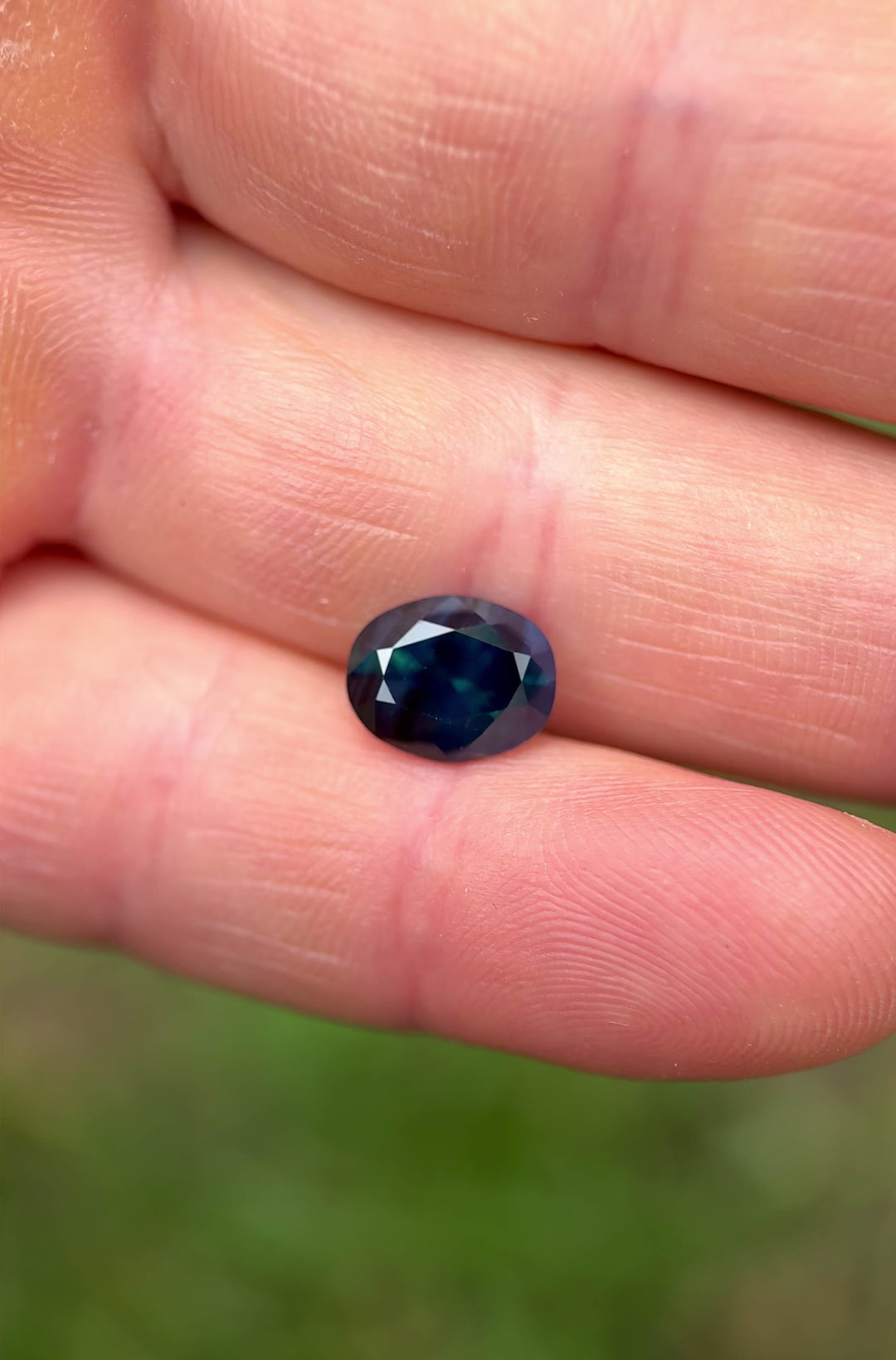 Dynamic hand-held video of an unheated oval sapphire from Nigeria, showcasing its rich peacock color and brilliant cut under natural light.