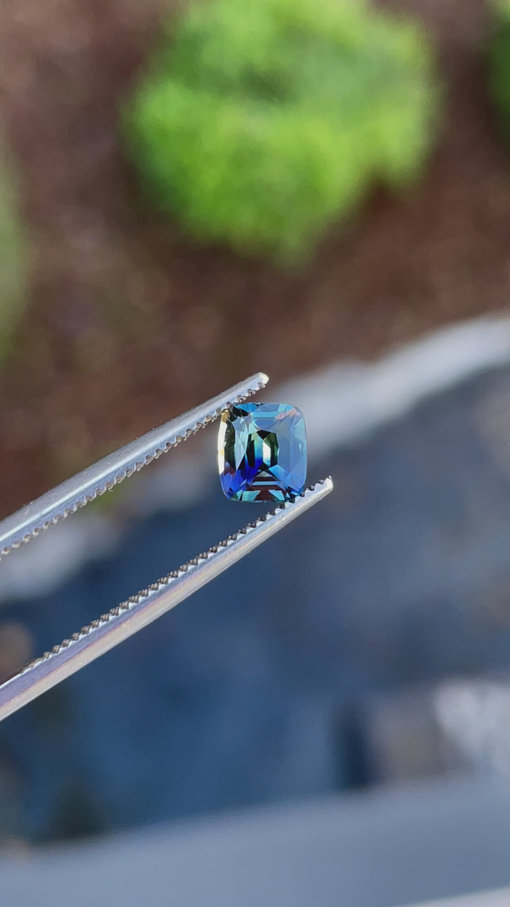 A mesmerizing 1.02-carat cushion-cut bi-color sapphire from Madagascar, shifting between vibrant blue and yellow hues under natural lighting.