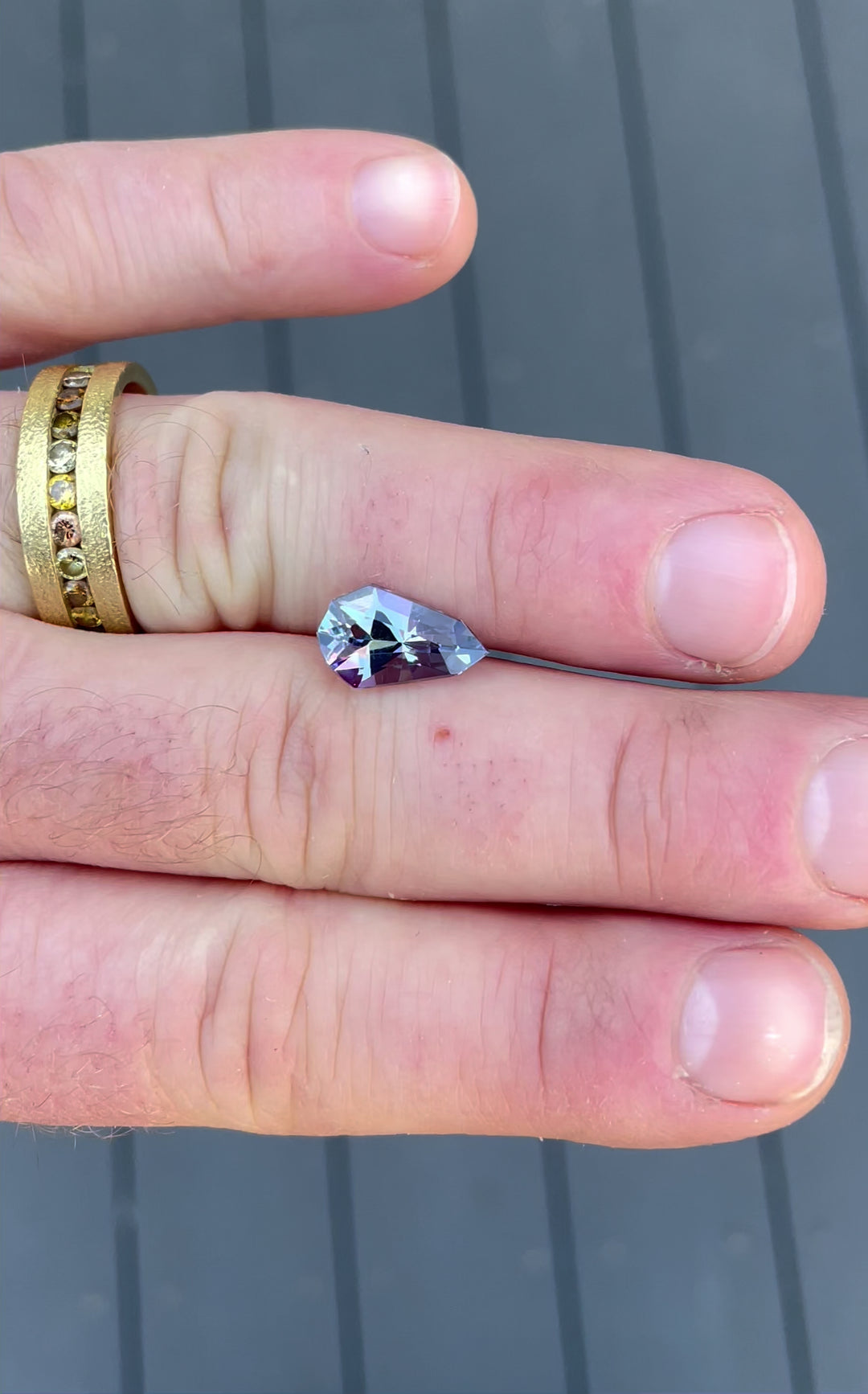 An intricate close-up view of a 3.31-carat tanzanite gemstone, showcasing its natural gray, blue, and purple hues with a geometric pear shape, untreated and ethically sourced from Tanzania.