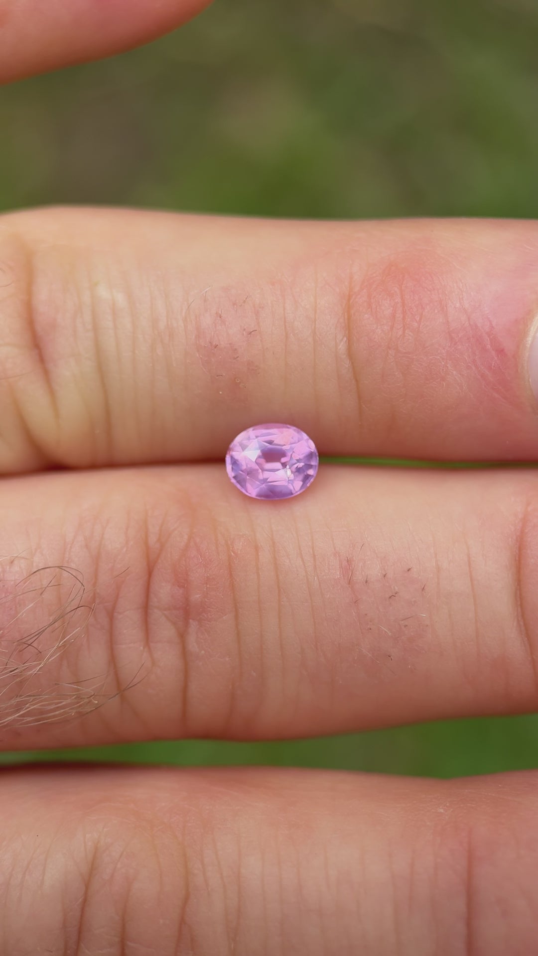 1.21 carat opalescent pink sapphire held between fingers with daylight reflection – oval mix cut from Ratnapura, Sri Lanka