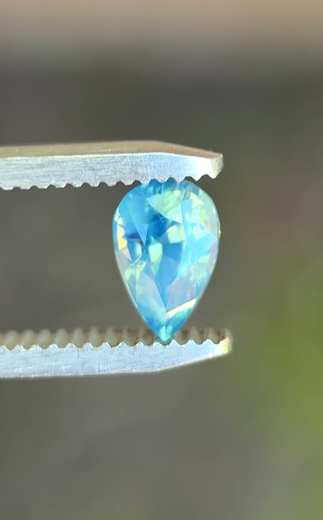 Natural Madagascar sapphire turning in tweezers, showcasing pear mixed cut symmetry and subtle teal-to-blue color movement under changing light.