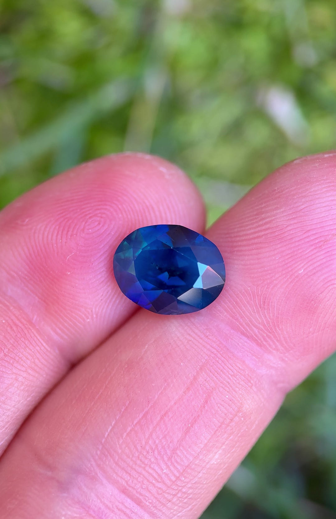 4.60ct unheated teal blue sapphire rotated in hand, revealing shifting royal blue and green flashes across brilliant facets.