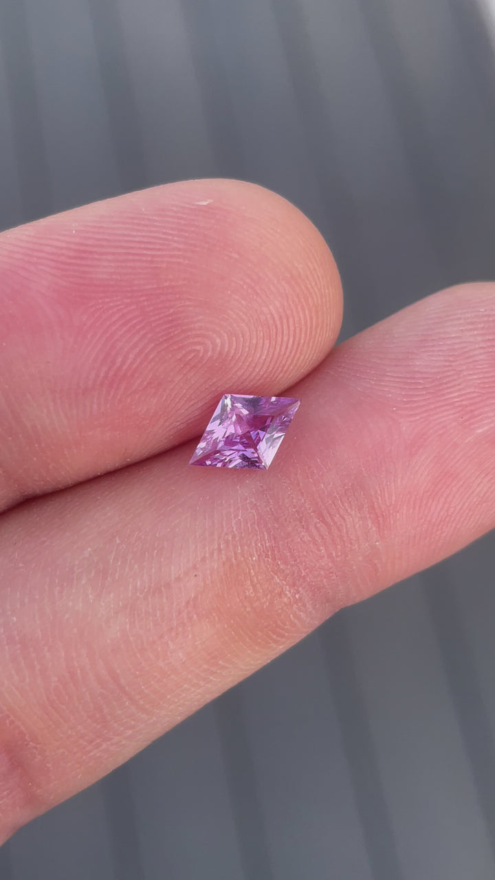 Close-up video of a 1.06-carat purple sapphire in kite step cut, rotating to capture its color play and precision. Originating from Sri Lanka and unheated, this sapphire shines with a distinct purple hue ideal for luxury jewelry.