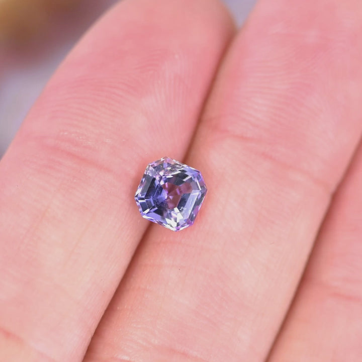 Close-up video of 1.14ct pink purple blue Tanzanite Asscher cut resting on hand, untreated precision faceted gemstone from Tanzania displaying geometric symmetry and vibrant sparkle