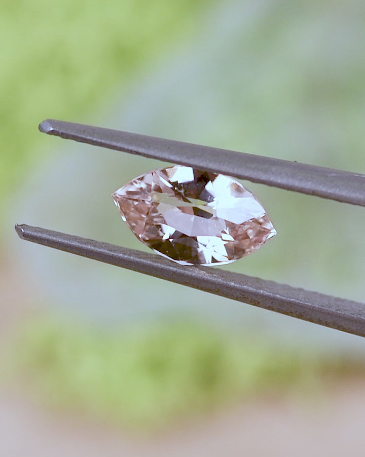 Video of 1.28CT peach sapphire rotating in gemstone tweezers under natural sunlight, revealing warm pastel tones, internal reflections, and the elegant faceting of the precision marquise mixed cut, untreated sapphire from Sakaraha, Madagascar