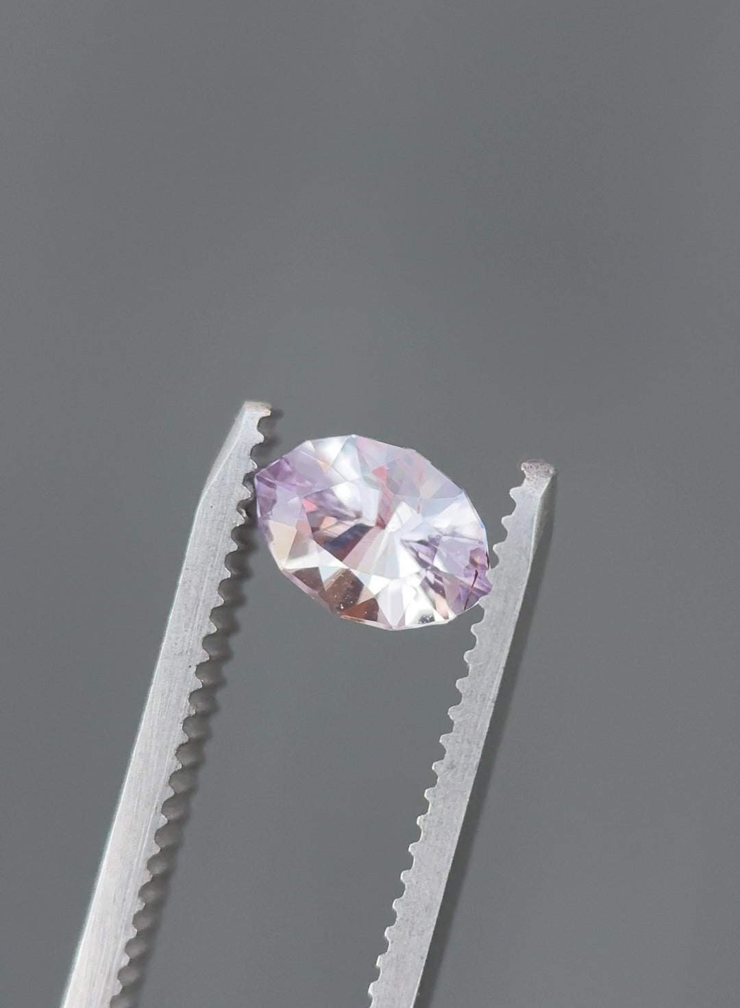 Video of 1.32CT pink, purple, and lilac sapphire rotating in gemstone tweezers under natural light, showcasing pastel color play, brilliance, and fine craftsmanship of the precision marquise mixed cut, unheated sapphire from Sakaraha, Madagascar.