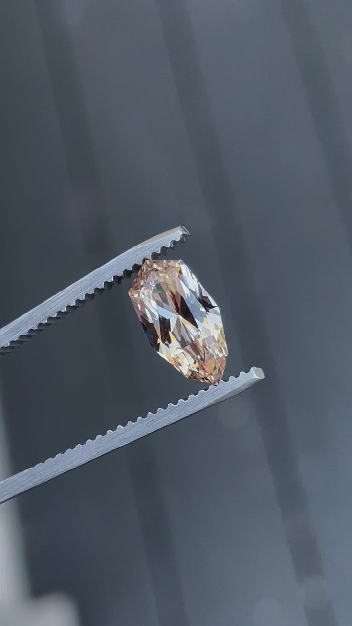 A rotating 2.07-carat peach and champagne sapphire with a custom geometric shield brilliant cut. The video highlights the gemstone's vibrant tones and intricate facets as it moves. The sapphire, untreated, measures 11.02mm by 5.87mm by 3.94mm and comes from Sri Lanka.