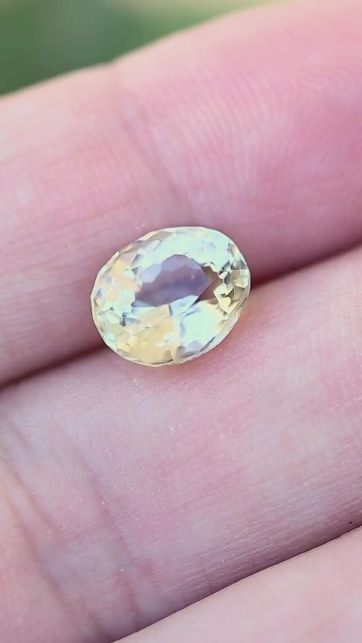 Untreated 2.34 carat butter yellow tourmaline shown moving on a hand in natural light, revealing its size, vintage oval silhouette and soft creamy yellow brilliance.