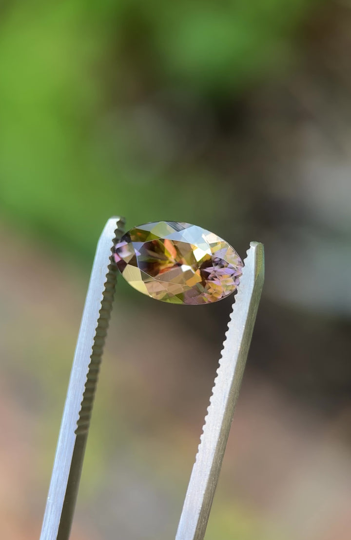 360-degree view of reddish orange Tanzanite in tweezers, showcasing color play and brilliance under sunlight