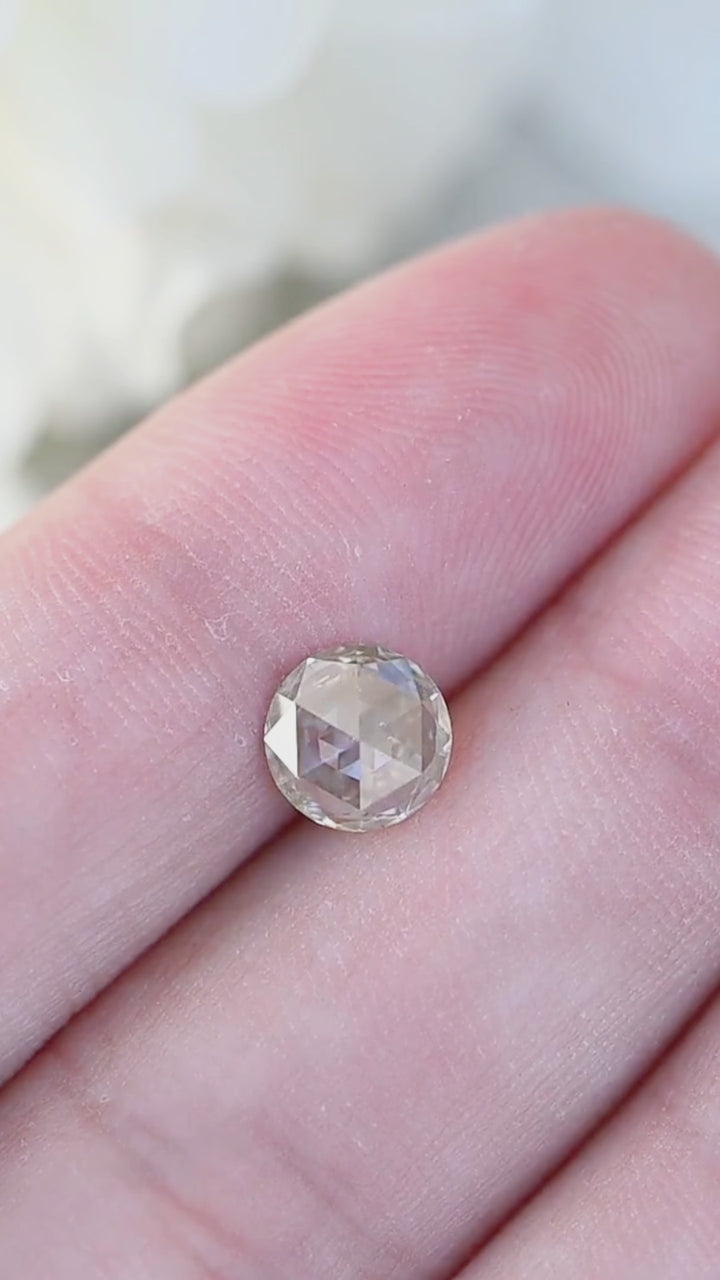 Video of a natural 1.00 carat grey champagne rose cut diamond displayed on fingertips, showing soft champagne-grey color and broad reflective antique facets in natural light.