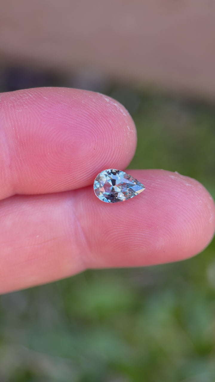 1.64ct unheated periwinkle sapphire rotated in hand, showing shifting flashes of icy blue, pale violet, and bright white reflections across precision-cut facets.