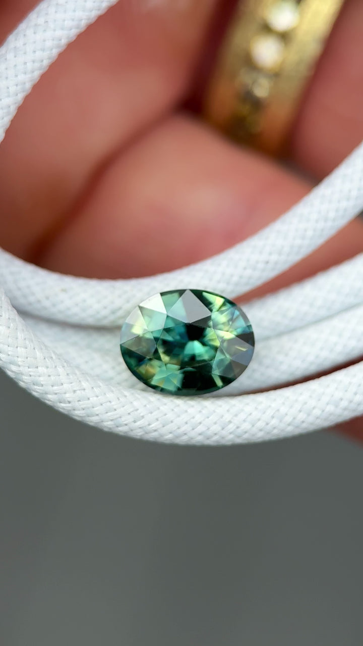 Rotating 3.02 carat yellow teal blue green parti sapphire in precision oval mixed cut, showing full color play and brilliance under natural light.