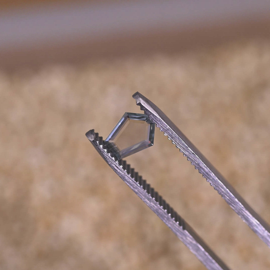 Loose green, blue and teal Montana sapphire rotating in tweezers, showing the thin portrait profile, crisp facet edges and natural Montana color in motion.