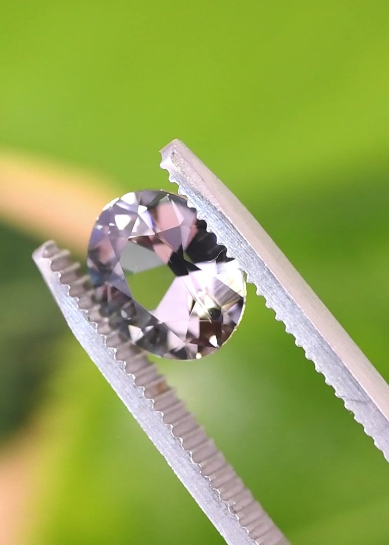 Handheld video of an untreated 2.57 carat Tanzanite in tweezers, showcasing facet reflections, depth, and a slightly subdued teal blue lavender color blend in a custom brilliant oval cut from Tanzania