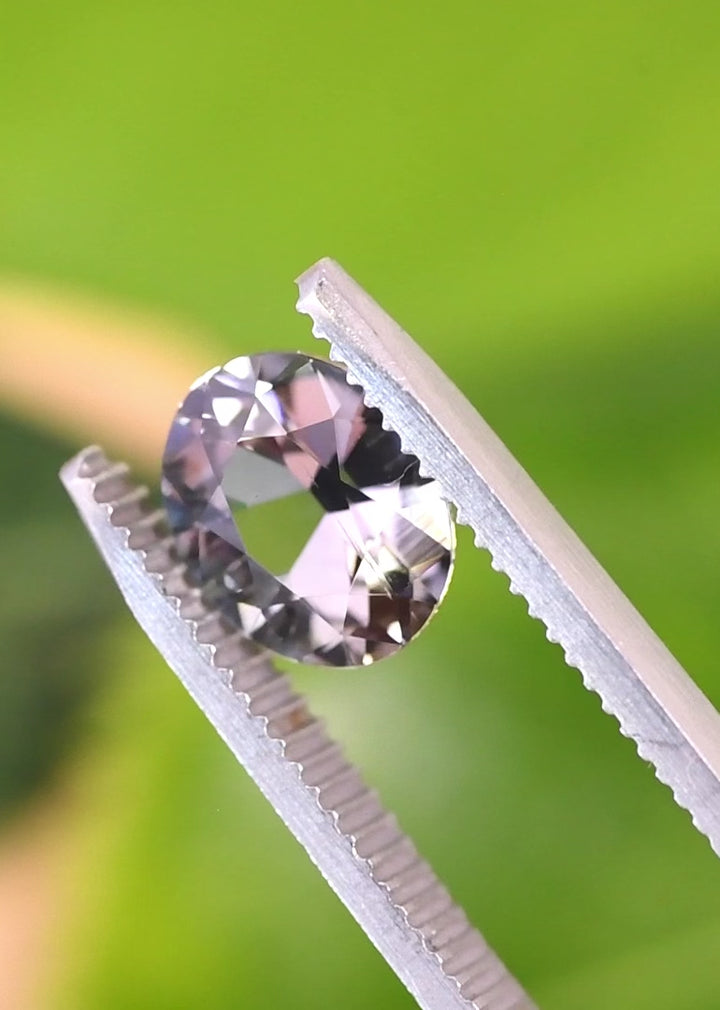 Handheld video of an untreated 2.57 carat Tanzanite in tweezers, showcasing facet reflections, depth, and a slightly subdued teal blue lavender color blend in a custom brilliant oval cut from Tanzania