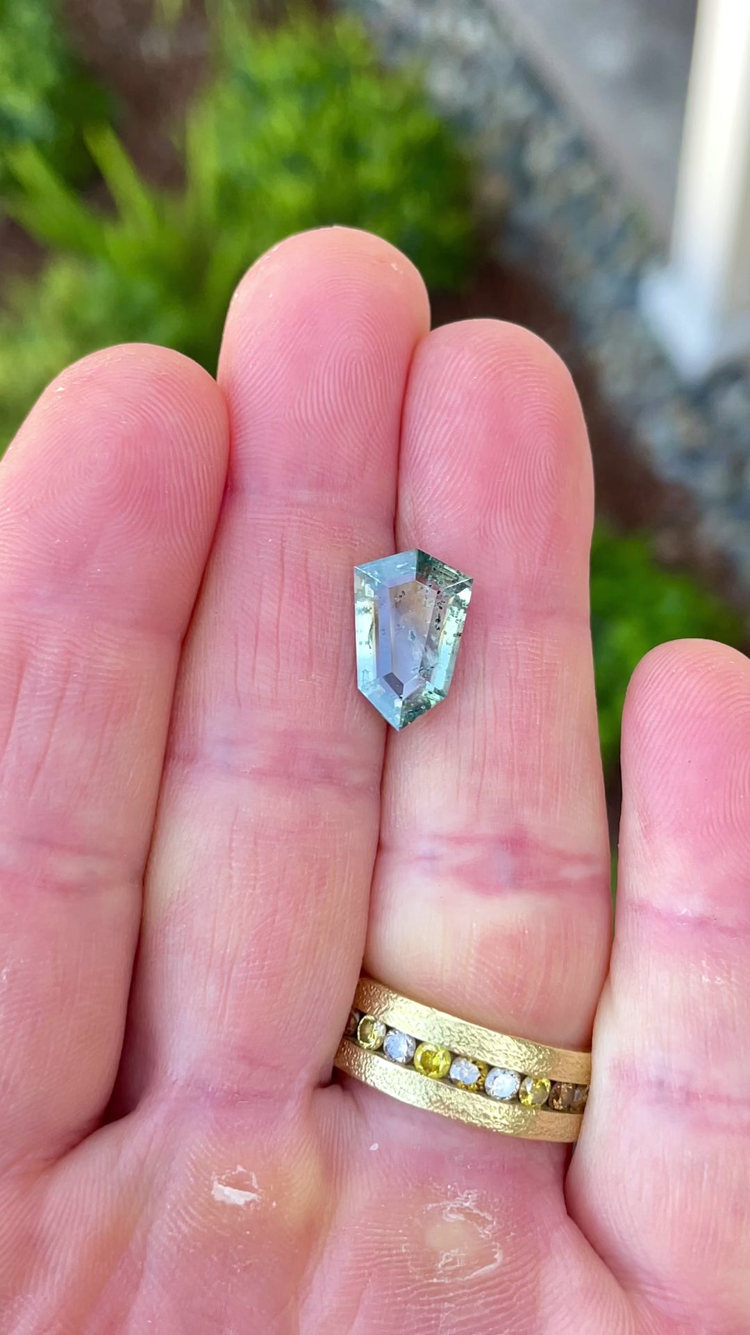 Video capturing the natural brilliance and internal features of a 5.48ct yellow, teal, and blue sapphire in outdoor lighting.