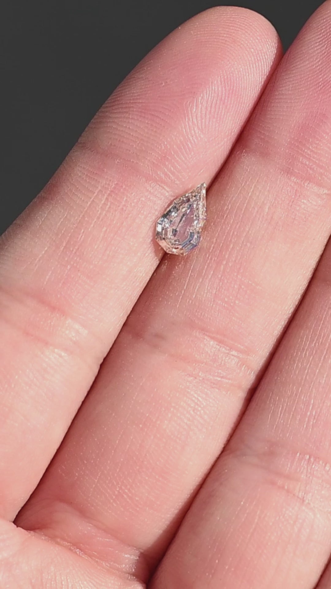 0.89ct Geo Pear Step Cut Champagne Diamond rotating on fingertips under direct sunlight showing off sparkle and size.