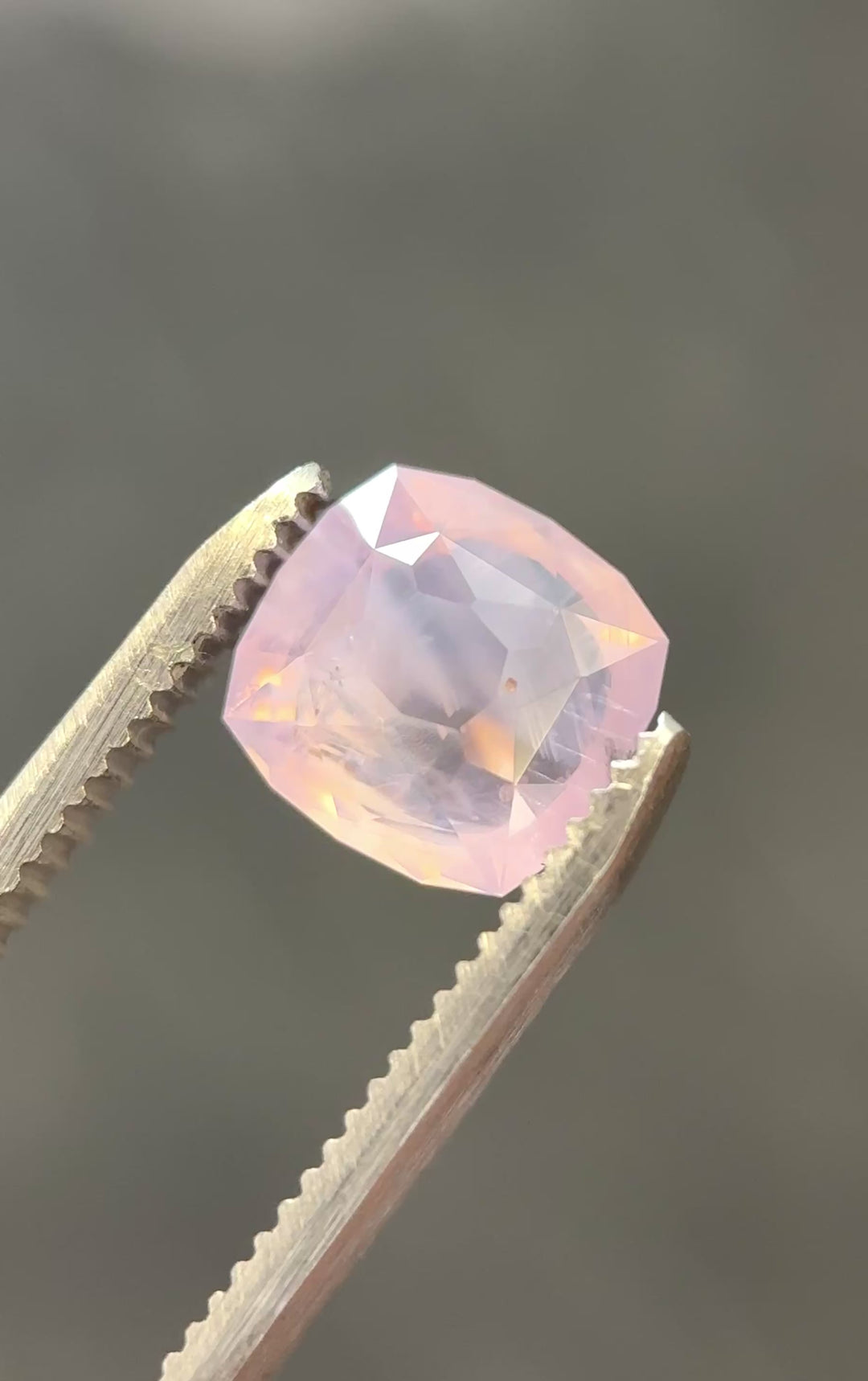 Ballet pink opalescent sapphire rotating in gem tweezers showing off whispy inclusions and natural opalescence.