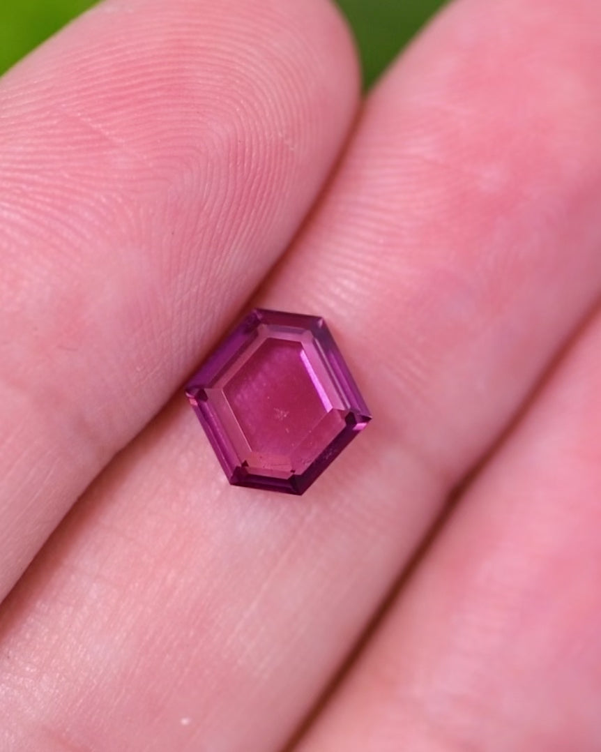 Macro video of 1.71 carat pink purple garnet resting on fingers, revealing reflective light play and vivid tones across the precision step cut tablet, unheated garnet from Kenya.