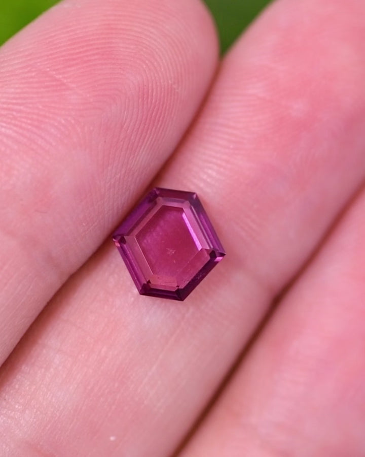 Macro video of 1.71 carat pink purple garnet resting on fingers, revealing reflective light play and vivid tones across the precision step cut tablet, unheated garnet from Kenya.