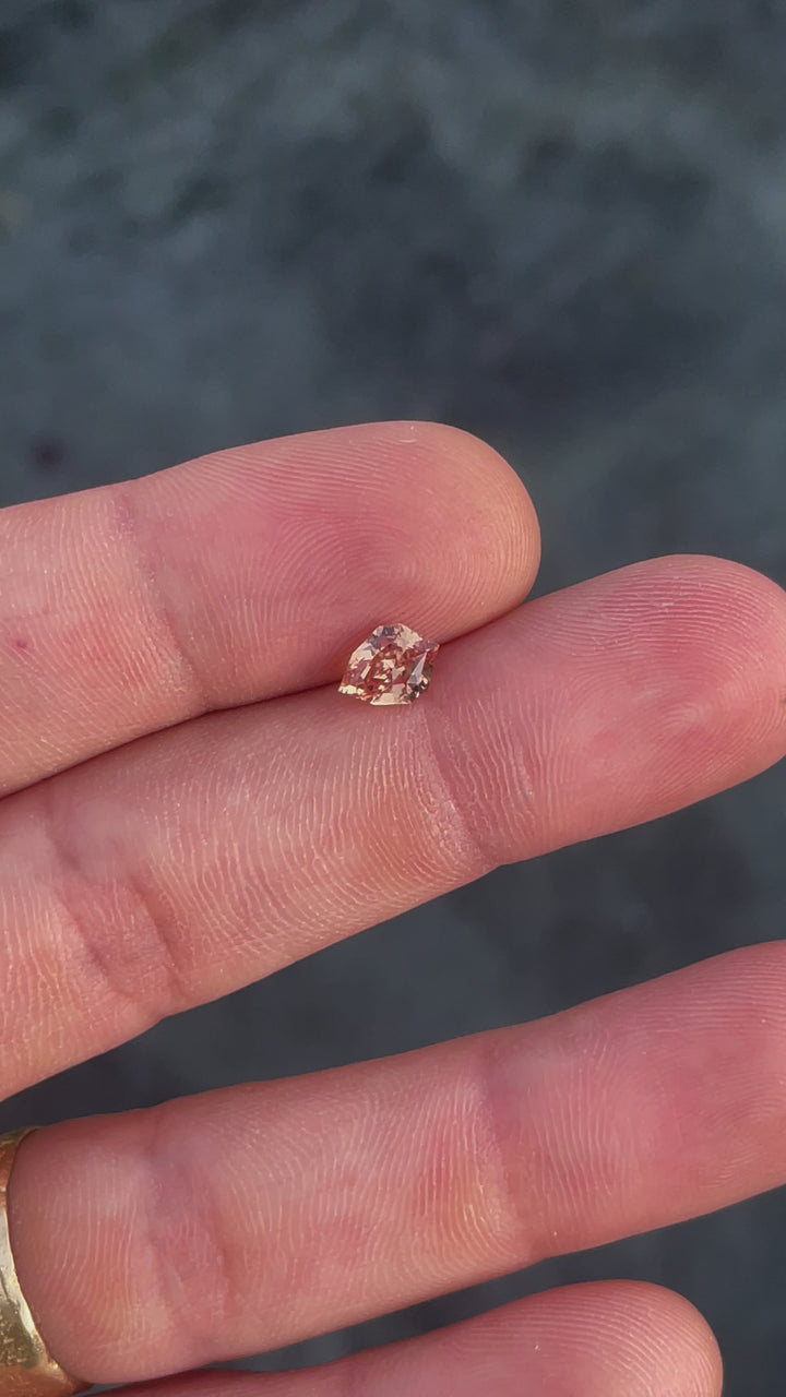 This video features a close-up of a 1.59-carat sapphire with a custom geometric shield cut, highlighting its orange and brown tones. As the gemstone is tilted and turned, the light captures the depth and warmth of its color.