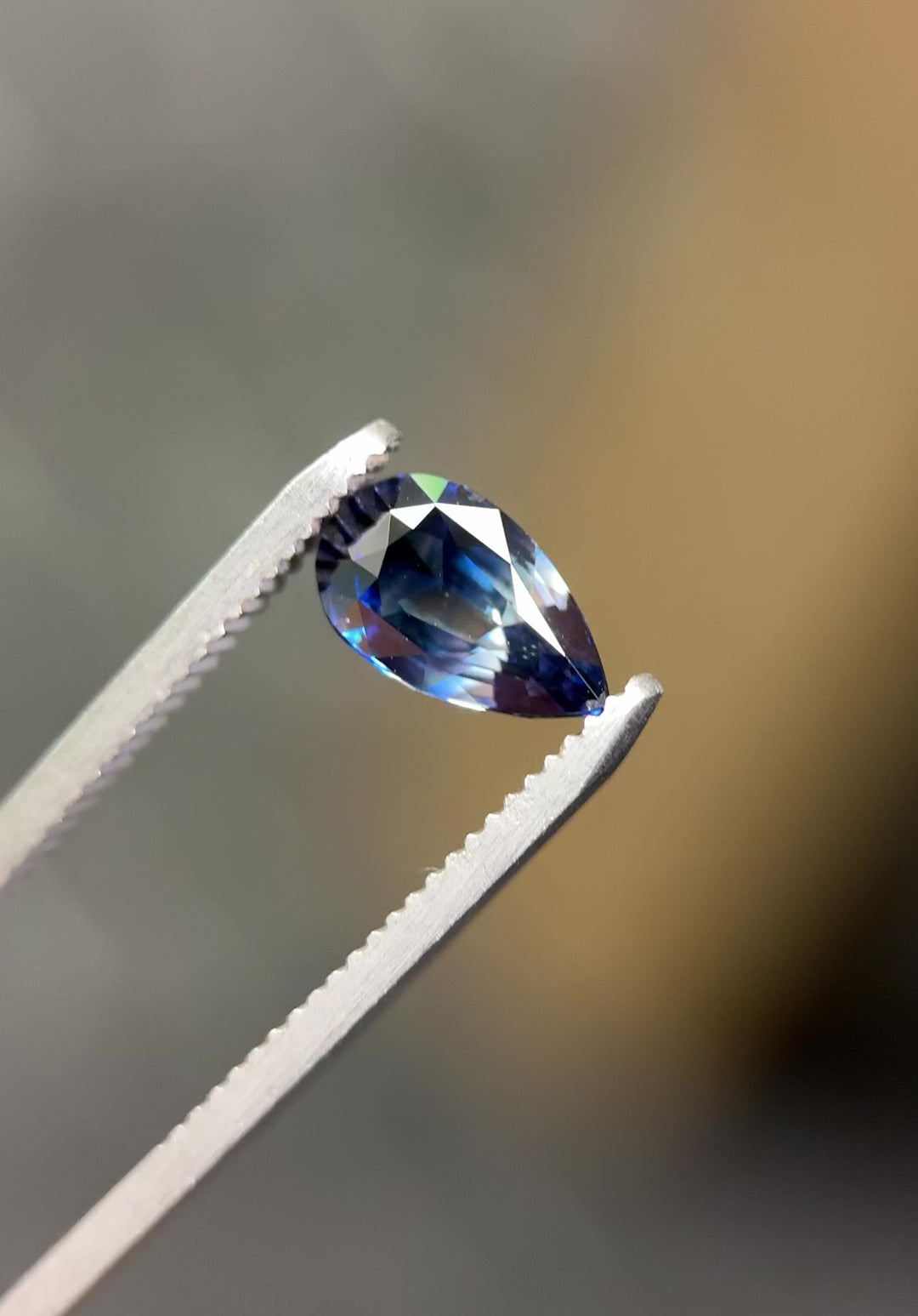 Video of 2.02CT bi-color blue sapphire rotating in gemstone tweezers under natural light, revealing vivid color shifts and scintillation from the pear brilliant cut, natural unheated sapphire from Sakaraha, Madagascar.