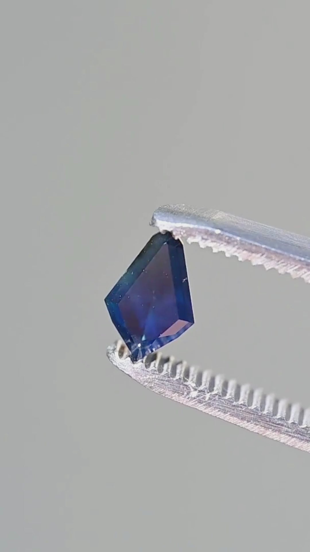 Explore the geometric step facets, rich navy-blue body color and cobalt reflections of this untreated 1.21ct Australian kite-shaped sapphire in a close-up tweezer view.