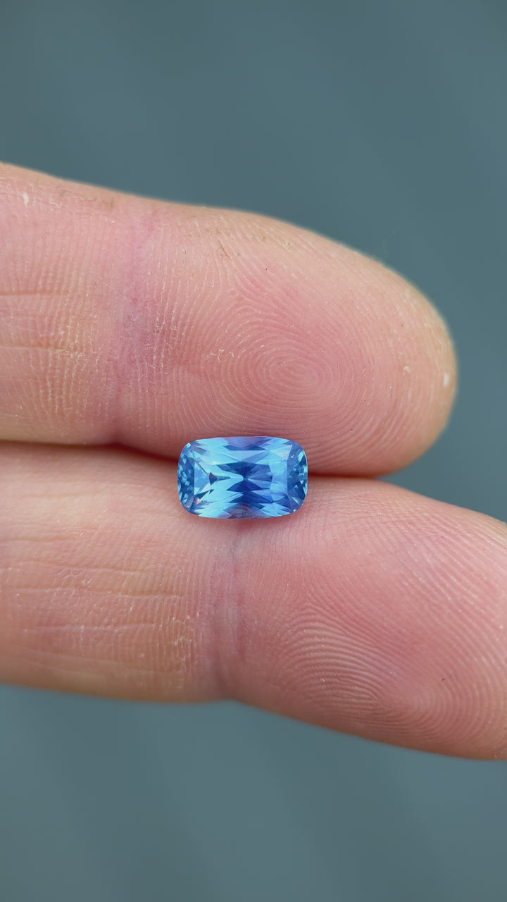 Hand-held movement video of 2.30CT cornflower blue sapphire, capturing sparkle, step-cut patterns, and vibrant unheated Madagascar hue as light shifts.