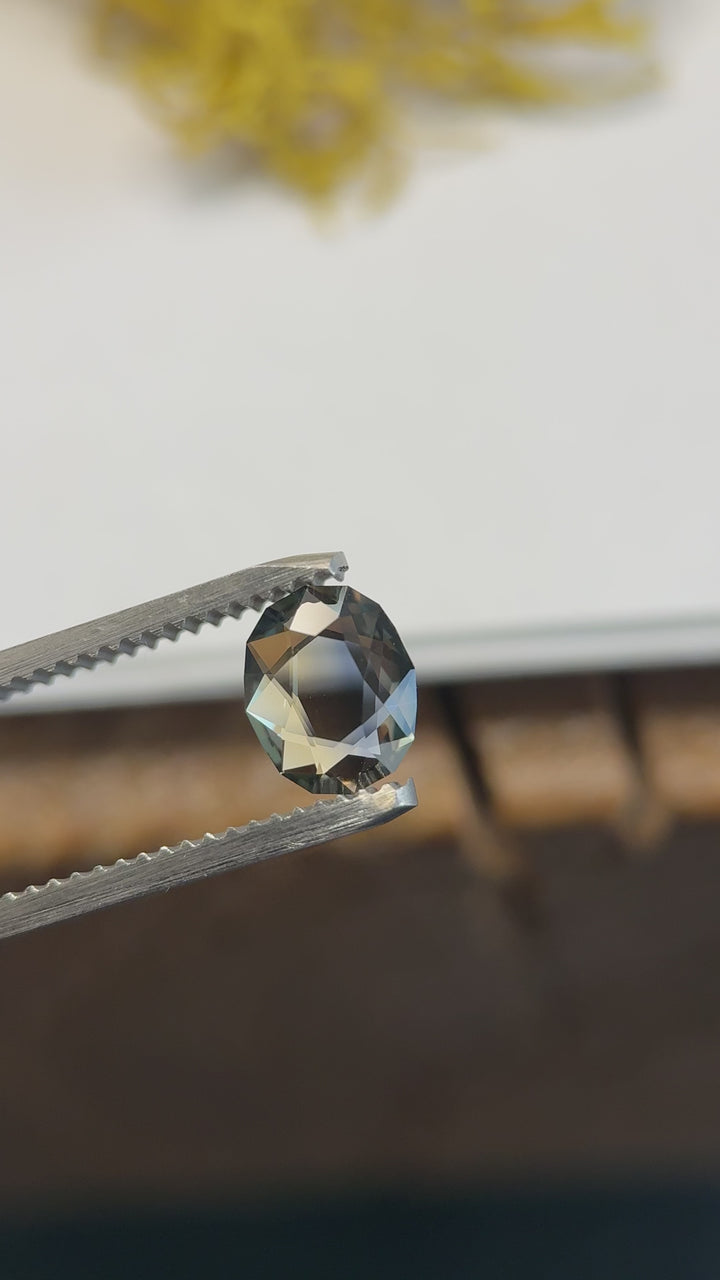 Blue and yellow oval portrait cut parti sapphire rotated in natural light, showing shifting contrast between deep midnight blue and glowing honey-yellow zones with crisp geometric reflections.