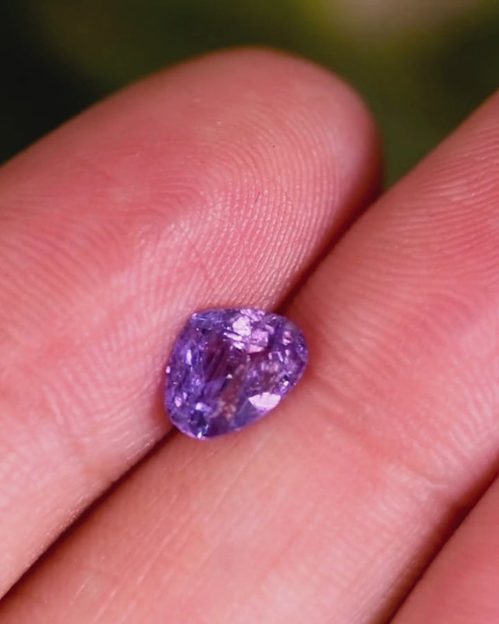 Video of 1.29CT violet lavender sapphire displayed on fingertip under natural light, showing shifting pastel hues and intricate brilliance of the trilliant modified brilliant cut, untreated gem from Umba River, Tanzania.
