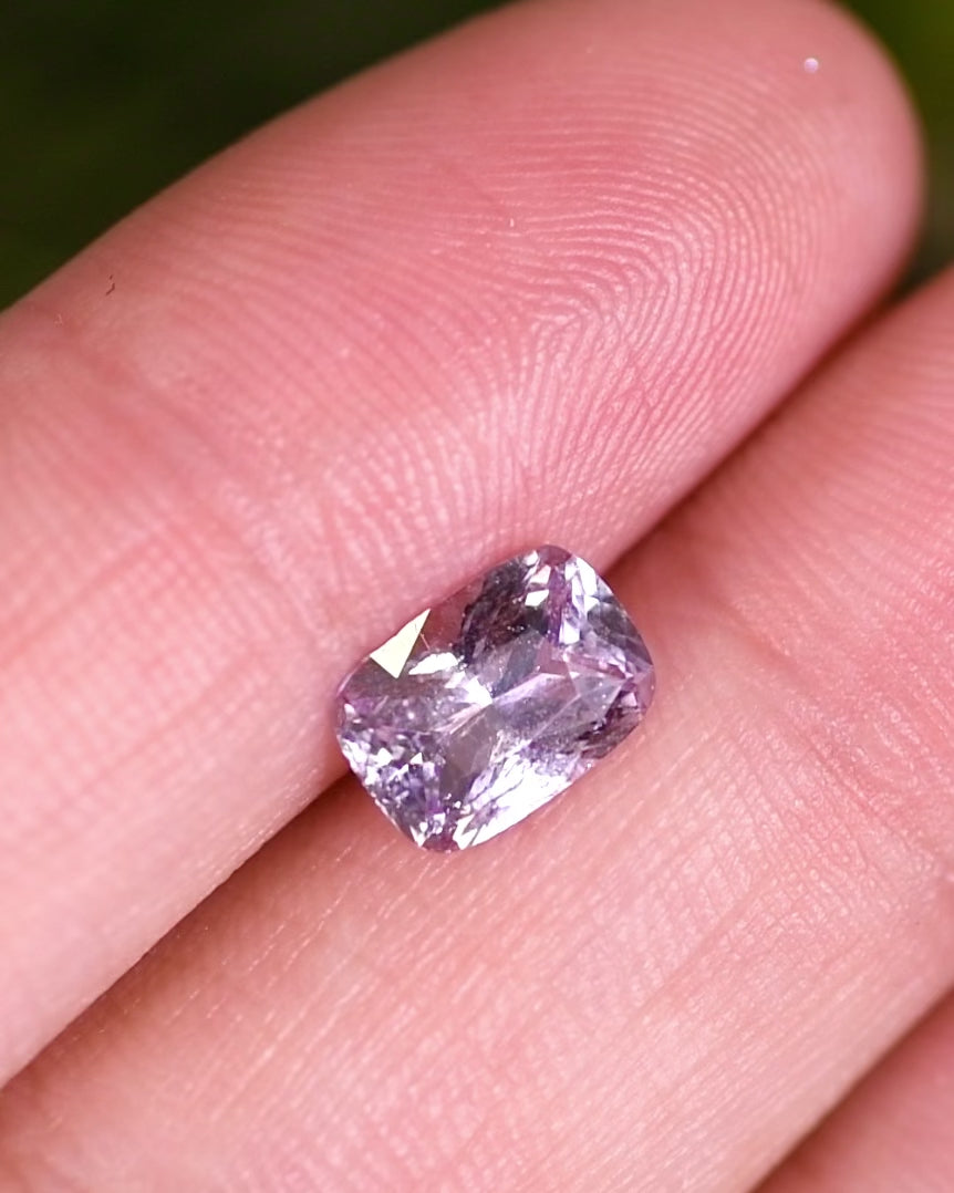 Close-up video of 1.65 carat sapphire resting on fingertips, reflecting soft violet and pink hues through the cushion brilliant cut facets, unheated gemstone from Madagascar.