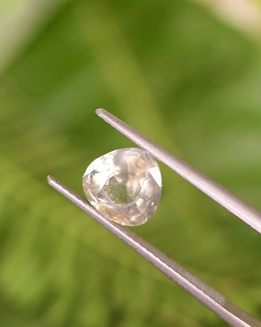 Video of 1.94CT yellow teal green sapphire rotating in gemstone tweezers under natural light, showcasing its vibrant play of color and craftsmanship in a custom portrait pear cut, untreated sapphire from Umba River, Tanzania.