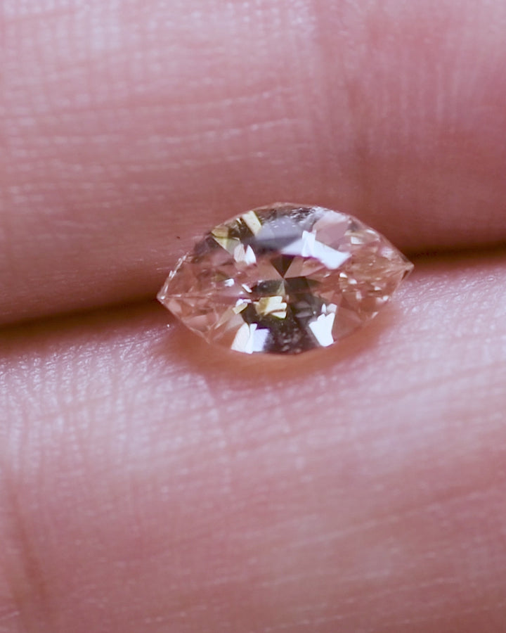 Close-up video of 1.28 carat peach sapphire resting on fingertip, capturing light play, shimmer, and brilliance from the precision marquise mixed cut, unheated sapphire from Sakaraha, Madagascar.