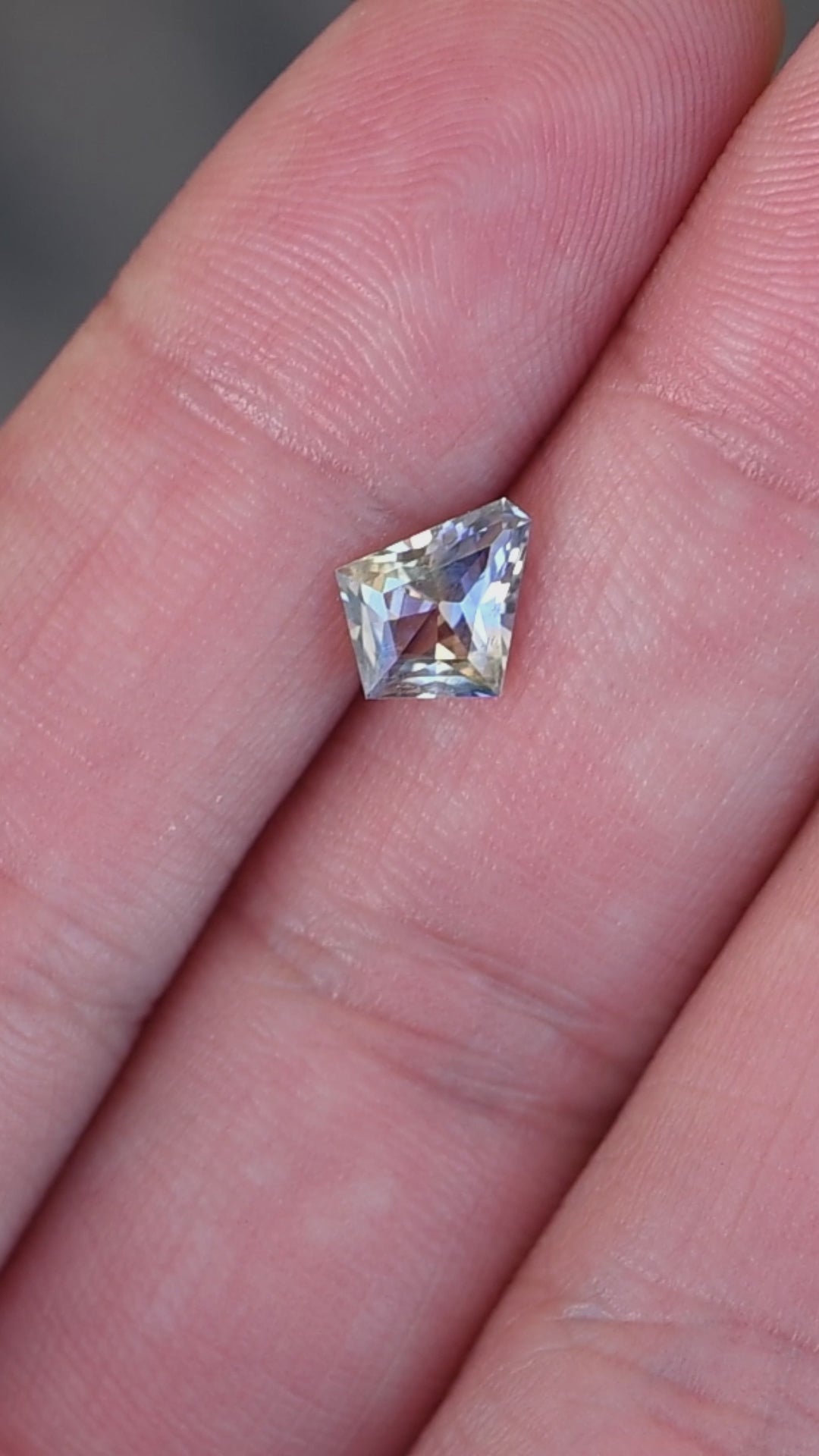 1.20ct Blue Yellow Parti custom kite cut sapphire rotating on fingertips under natural light.