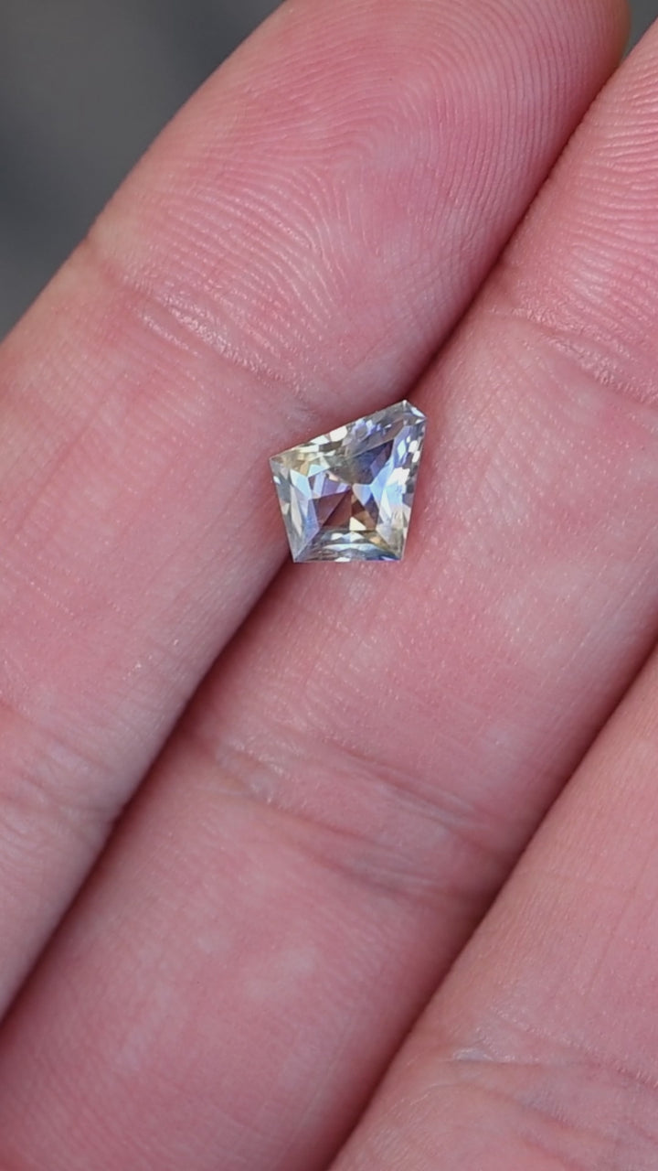 1.20ct Blue Yellow Parti custom kite cut sapphire rotating on fingertips under natural light.