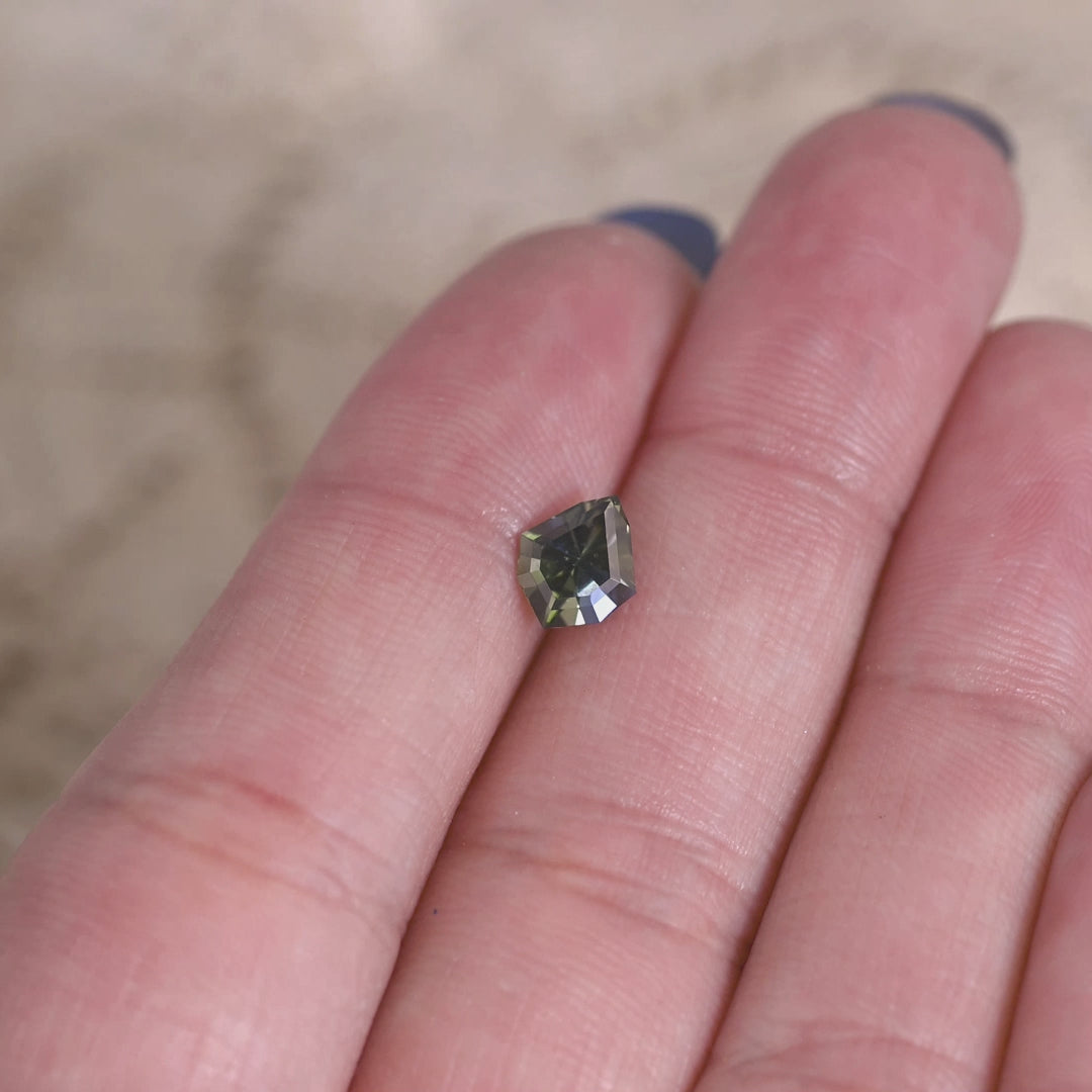 Teal blue green tanzanite gemstone displayed on a hand showing the custom geometric shield cut and natural brilliance of the stone.