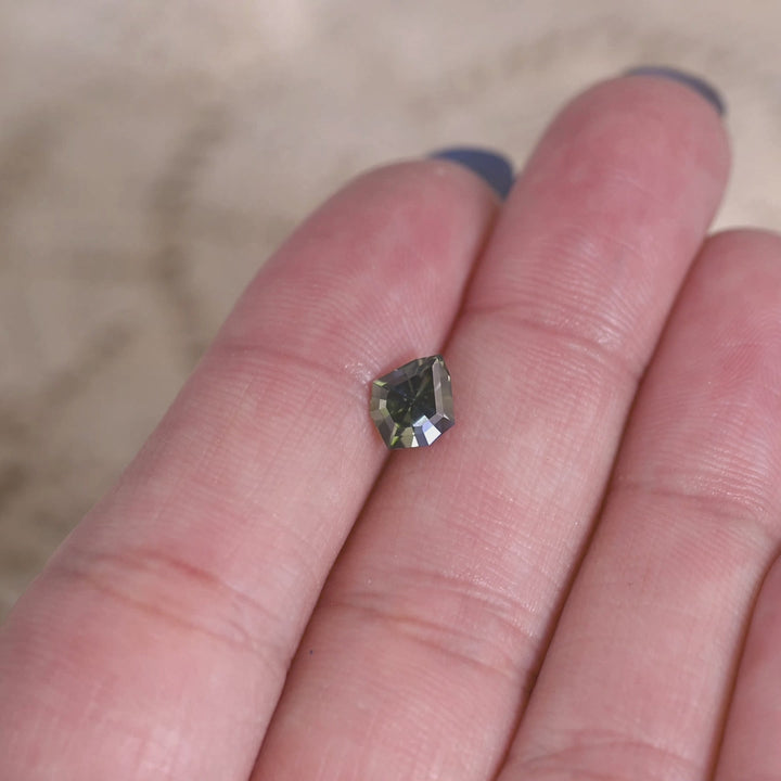 Teal blue green tanzanite gemstone displayed on a hand showing the custom geometric shield cut and natural brilliance of the stone.