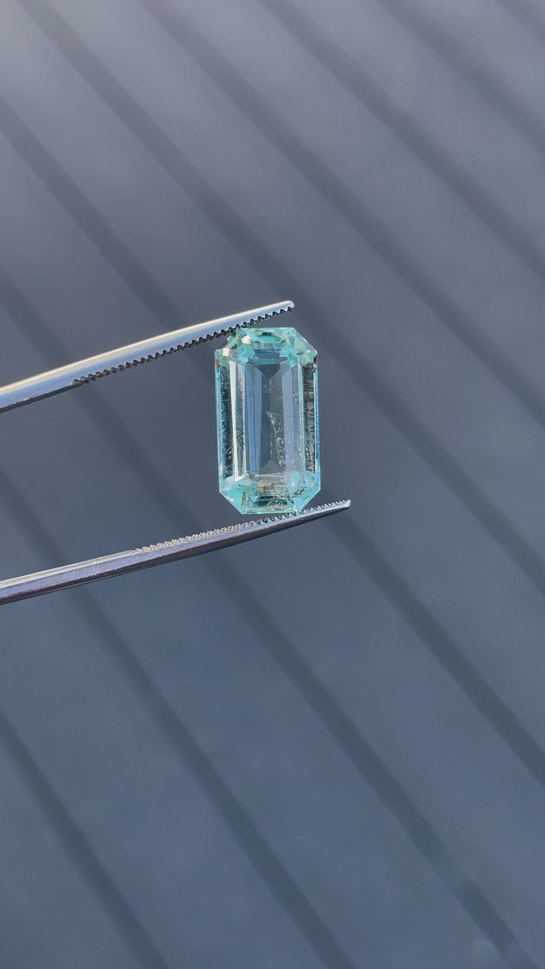 Rotating view of an 8.80-carat aquamarine gemstone in tweezers, highlighting its emerald cut and mint blue-green tones.