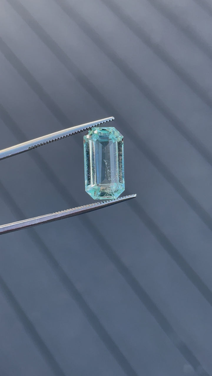 Rotating view of an 8.80-carat aquamarine gemstone in tweezers, highlighting its emerald cut and mint blue-green tones.
