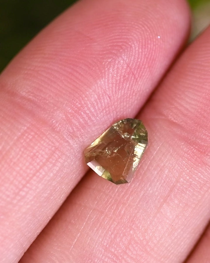 Close-up motion video showing 1.01 carat sapphire turning under natural light, displaying yellow, teal, and green hues with detailed facets of its custom shield portrait cut, ethically sourced unheated gem from Umba River, Tanzania.