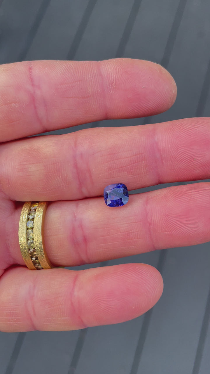 A 1.82-carat smokey lavender and violet sapphire shown under natural lighting to highlight its cushion cut and vibrant parti color play.