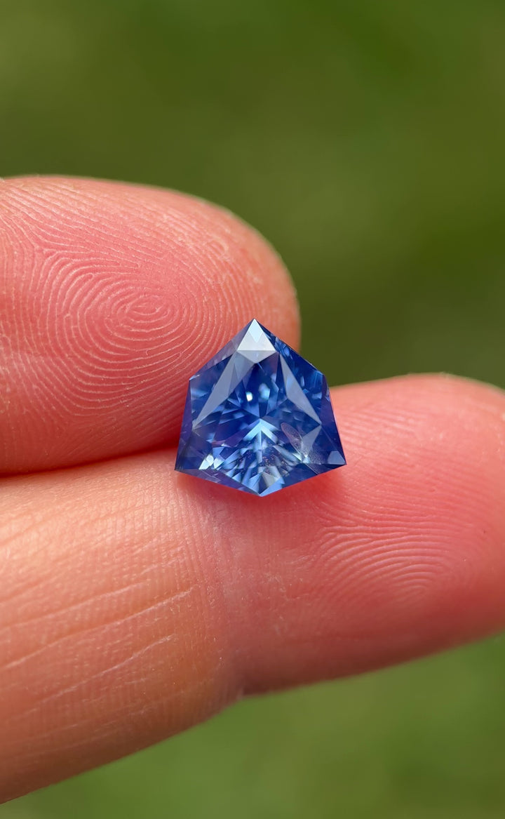 Video of 5.10CT vibrant bright blue sapphire rotating in gemstone tweezers, showcasing brilliance, clarity, and dynamic light return of the precision custom trillion shield mix cut, unheated sapphire from Sakaraha, Madagascar.