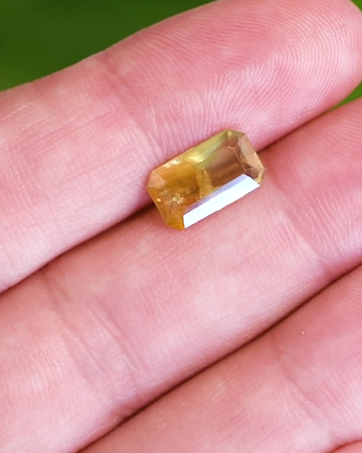 Video of 2.74 carat parti sapphire resting on fingertip, showing shifting colors of green, yellow, and orange as light moves across the custom octagonal step cut, untreated sapphire from Umba River, Tanzania.