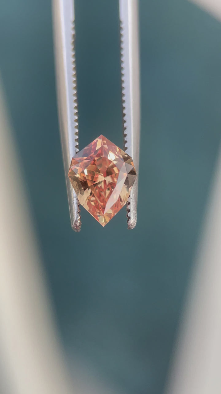 A mesmerizing video of a 1.59-carat orange-brown sapphire from Sri Lanka, set against a natural background. The custom geometric shield cut sparkles as the gemstone is rotated, revealing its intricate faceting and the play of light within its warm hues. This untreated sapphire is an exquisite display of natural beauty.