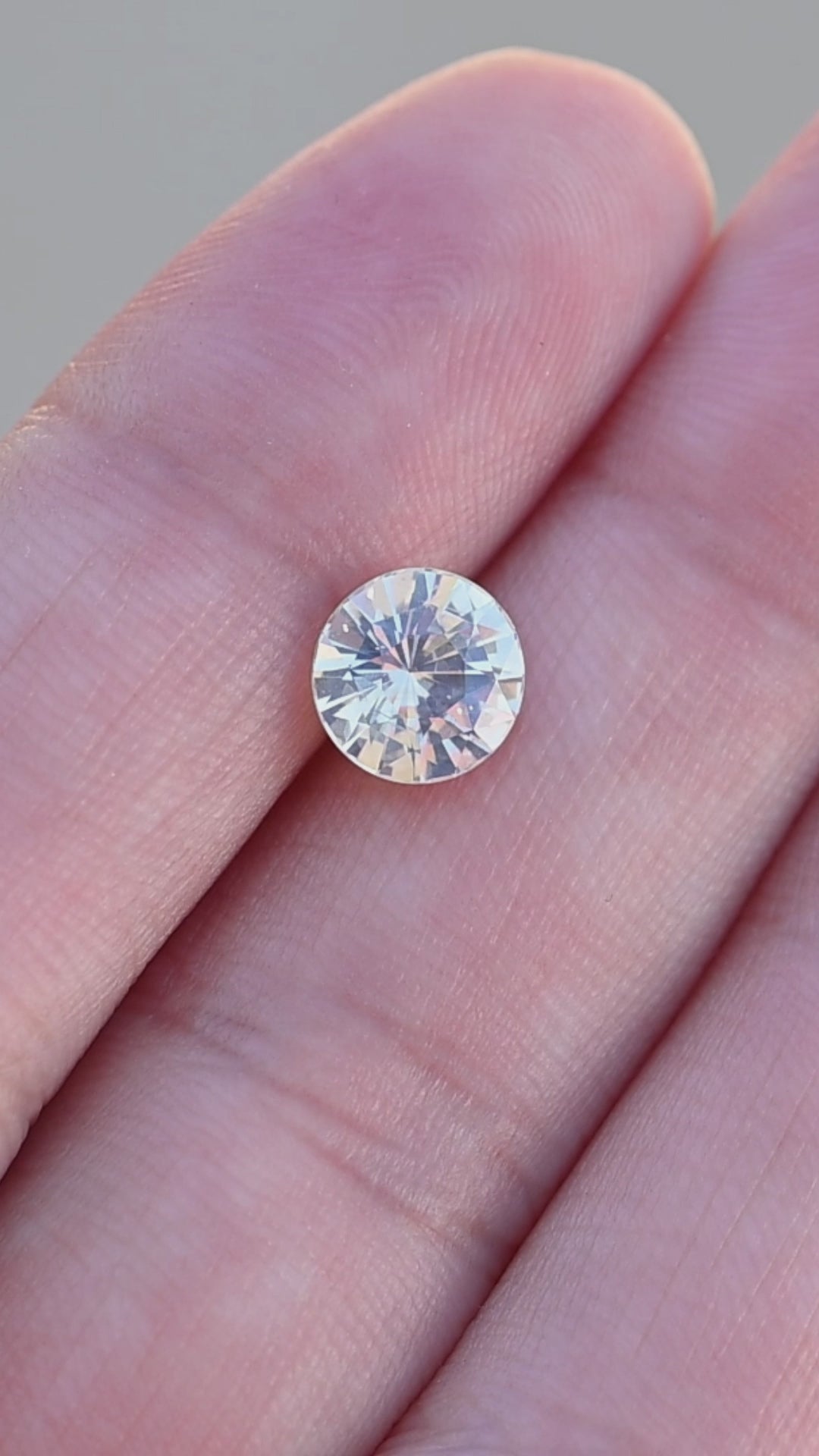 Natural round white opalescent sapphire rotating on finger tips showing off natural glow.