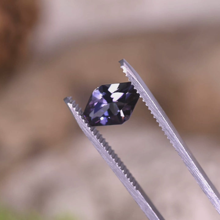 Close-up video of 2.19ct peach lavender blue Tanzanite asymmetrical octagon held in tweezers, designer precision cut gemstone from Tanzania displaying sharp geometry, sparkle and multicolor light performance
